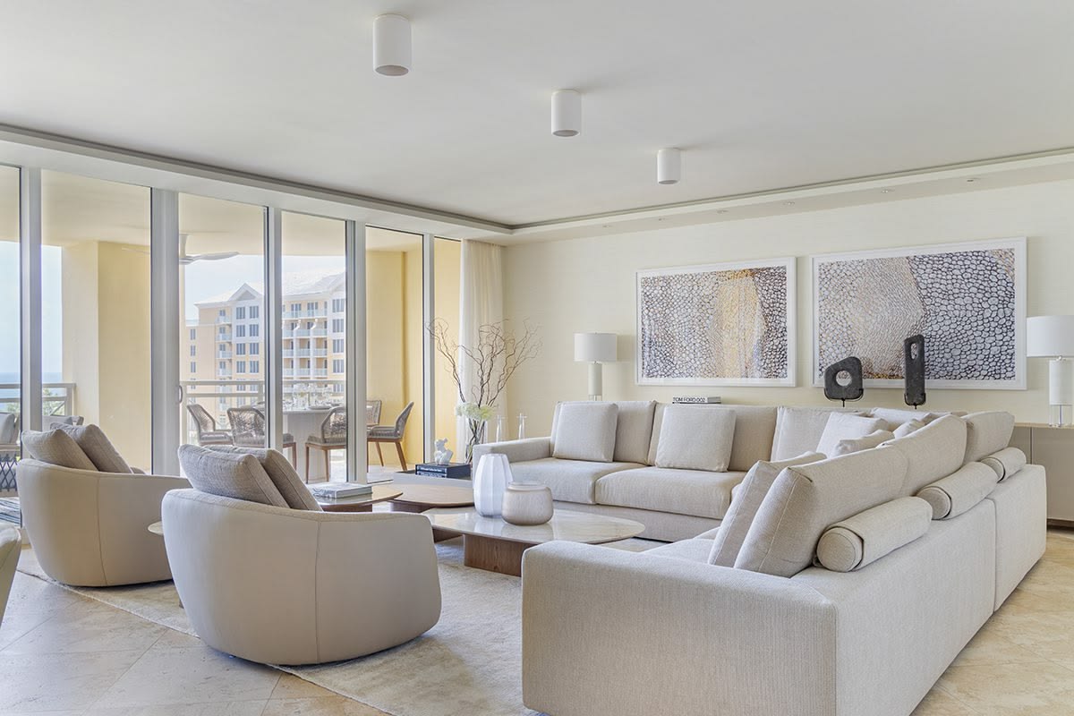 Modern living room with beige sofa, armchairs, and large windows.