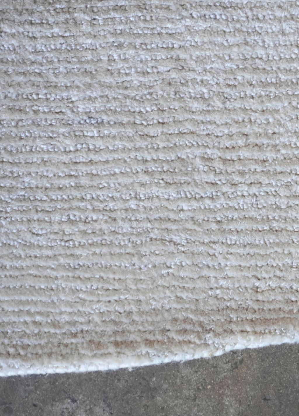 Close-up of a textured beige carpet bordering a concrete surface.