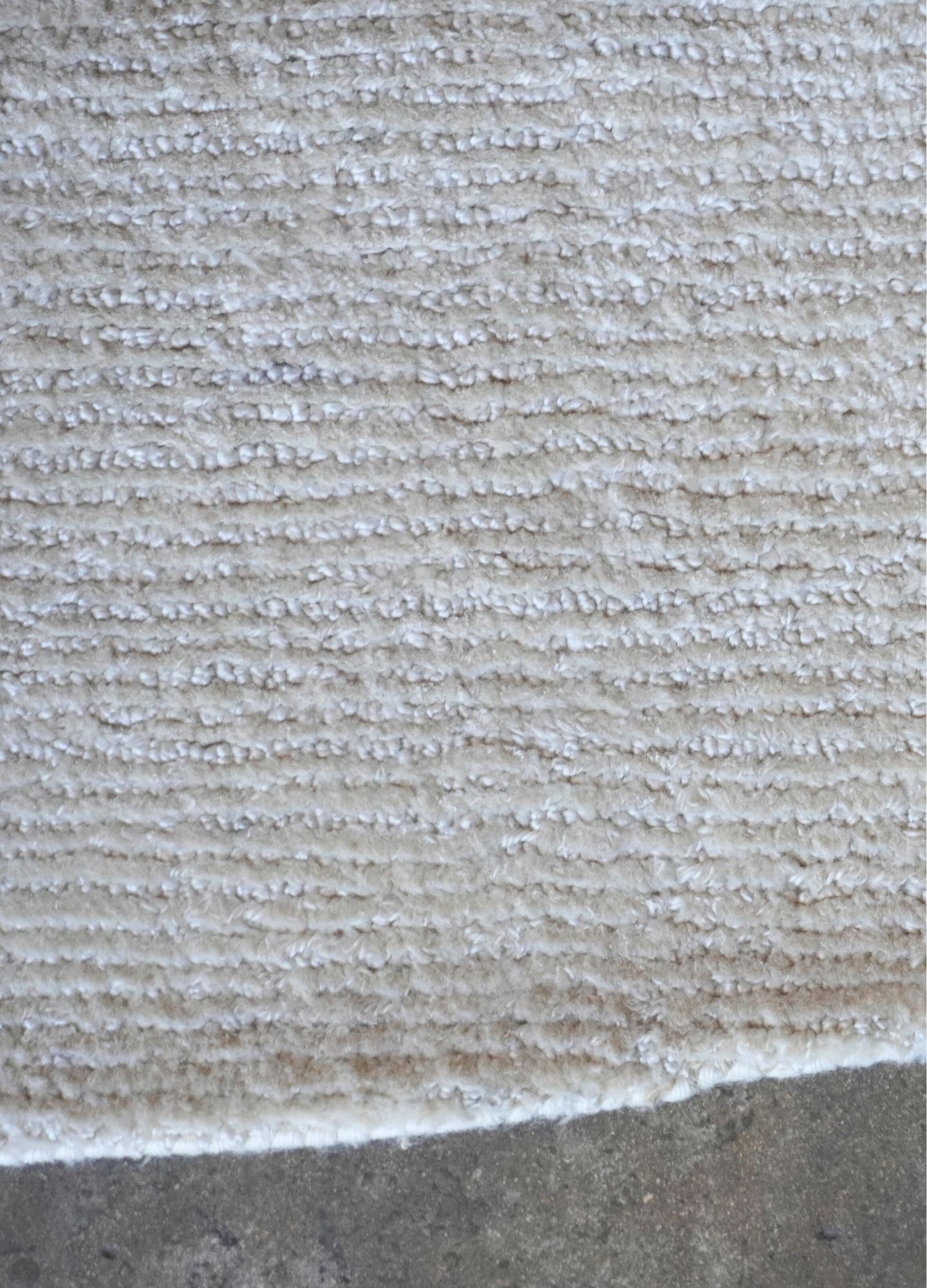 Close-up of a textured beige carpet bordering a concrete surface.